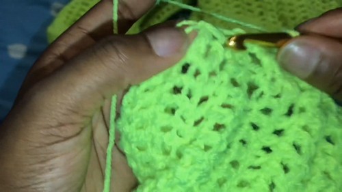 Close view of hands crocheting an open lace pattern in neon green yarn with a gold hook.