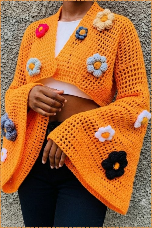 Finished crochet bell sleeve cropped sweater in orange mesh worn open over a white crop top, showing the full spread of puff flower embellishments in pink blue grey black and white.