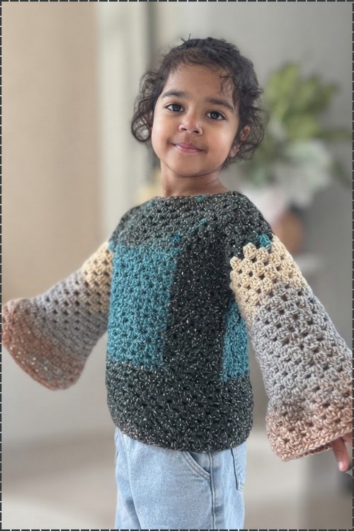 Finished crochet bell sleeve sweater on a toddler, showing the full width of the flared granny stitch sleeves from the back and side angle.