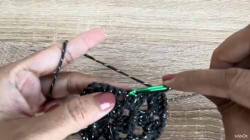 Attaching the teal accent edging at the neckline of the dark grey crochet sweater body, sleeve panel visible alongside.