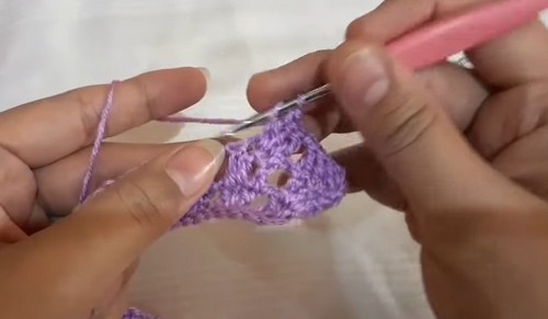 Working the early shell stitch repeats of the purple sweater collar with a pink hook, the fan shaped clusters just beginning to form.