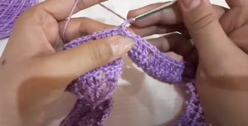 Completing a round of the purple shell stitch yoke section with a silver hook, the rounded collar shape accumulating.