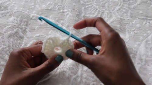 Hands working a crochet hook along the edge of a pink and white granny stitch panel in progress