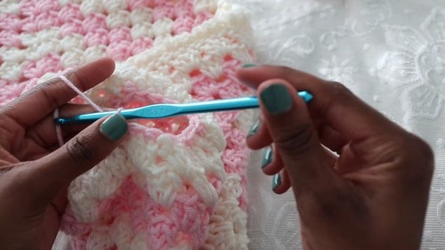 Close-up of hands crocheting into a pink and white granny stitch fabric panel with a teal hook