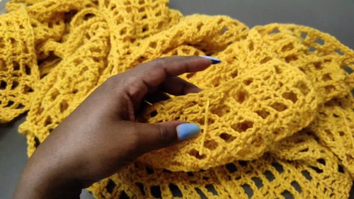 Hand lifting a section of finished yellow crochet mesh fabric showing the open v stitch lattice texture
