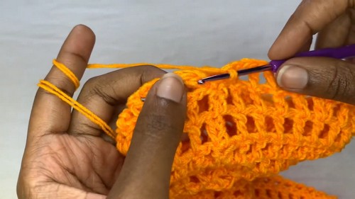 Continuing rows of the orange mesh sweater panel showing the regular chain and double crochet grid repeat.