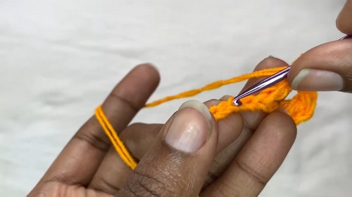 Starting the foundation stitches for the orange crochet sweater with a striped hook and bright orange yarn.