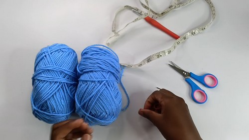 Two balls of blue yarn with a tape measure scissors and tapestry needle laid out as materials for the crochet bell sleeve sweater.