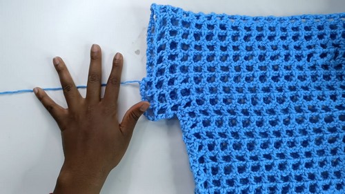 Completed blue mesh body panel laid flat beside a hand for scale, showing the consistent open grid repeat.