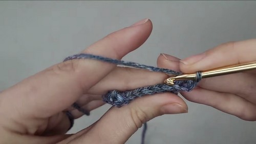 Hands working the foundation chain of a blue and pink variegated yarn with a gold crochet hook.