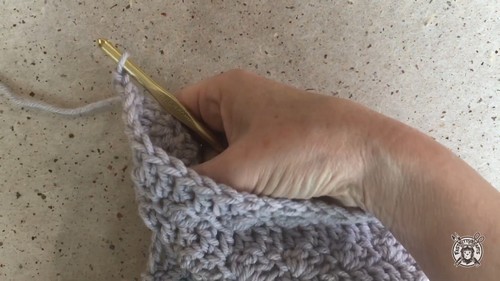 Working the diagonal armhole shaping on the grey crochet vest with a gold hook, the angled decrease edge clearly visible.