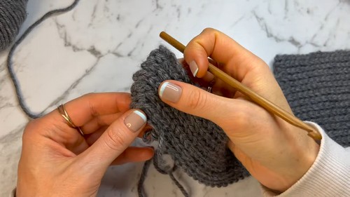 Hands working a gold hook through the edge of a grey ribbed crochet panel to pick up stitches along the side