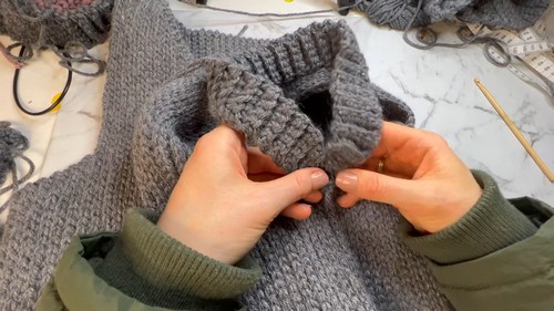 Hands pinning the shoulder seam of a large grey crochet vest panel before joining on a marble surface
