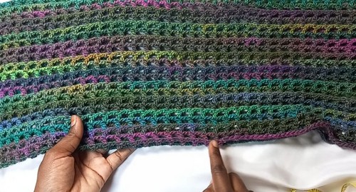 Hands holding a completed multicolor variegated crochet panel flat showing alternating solid and open filet rows.