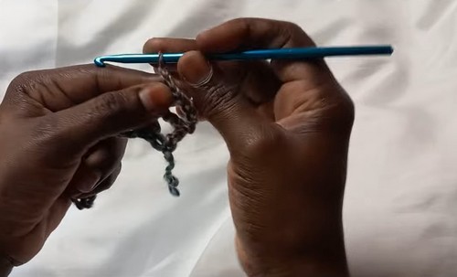 Hands working the foundation chain in multicolor variegated yarn with a blue hook on a white surface.
