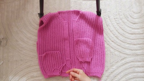 Completed pink crochet vest body with two patch pockets attached and front opening, pinned flat before finishing