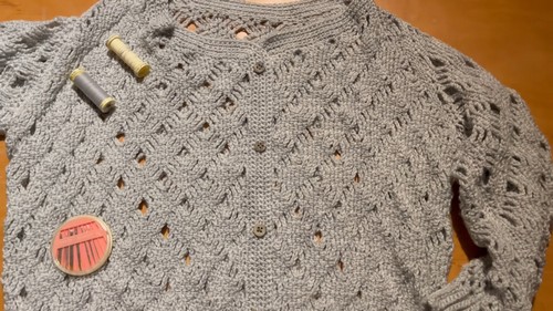 Finished gray crochet diamond lace cardigan laid flat showing buttons and needle and thread ready for finishing