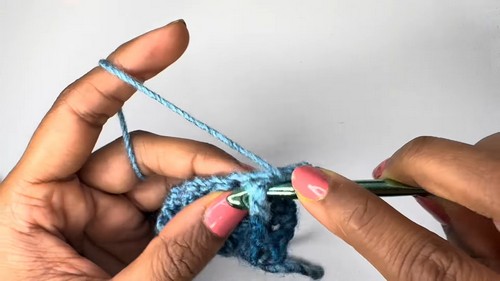 Close-up of a hand holding the assembled crochet sweater body showing blue and teal striped stitch rows