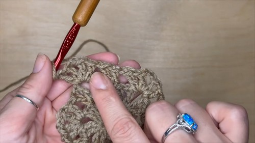 close-up of hands pointing to the v-stitch cluster structure of a beige hexagon motif with a red hook inserted