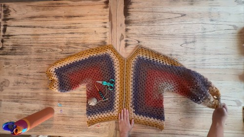 overhead view of two hexagon panels joined and laid out as a sweater shape with V-neck opening visible, tools resting on top