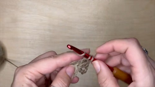 hands working a red crochet hook through beige yarn to begin a small hexagon motif on a wooden surface