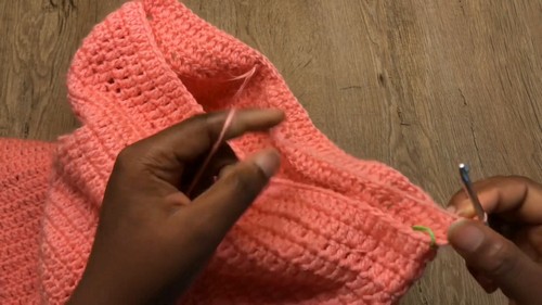 Coral crochet mesh body panel being seamed at the shoulder with a yarn needle