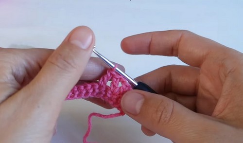Working the foundation neckband rows of the pink crochet collar with a silver hook, the first few stitches of the rib band forming.