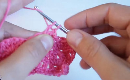 Working the shell scallop edging along the outer rim of the pink crochet collar, the fan clusters beginning to form.
