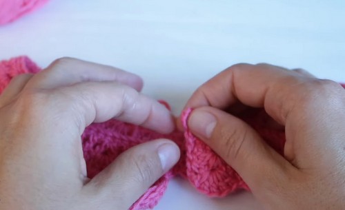 Folding and checking the finished pink crochet collar to assess how the scalloped edge lies flat before attaching the button.