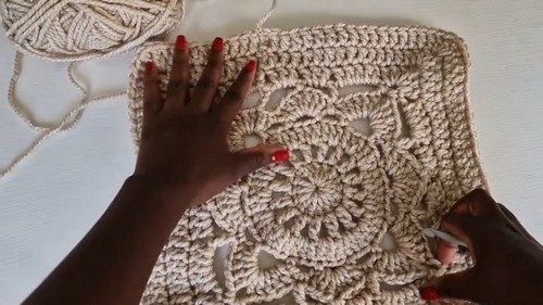 Hands pressing flat a large circular cream crochet motif on a white surface with a yarn ball nearby.