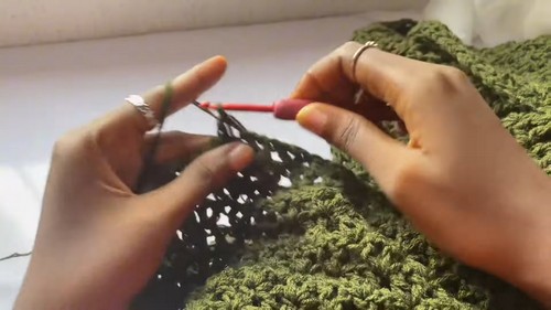 Hands working a red hook through an olive green crochet fabric showing the open lace star stitch pattern in progress