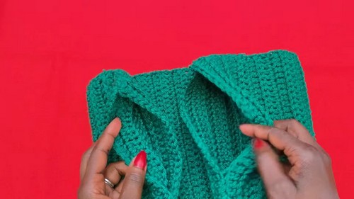 Completed green crochet sweater panels being folded and positioned to show the garment construction