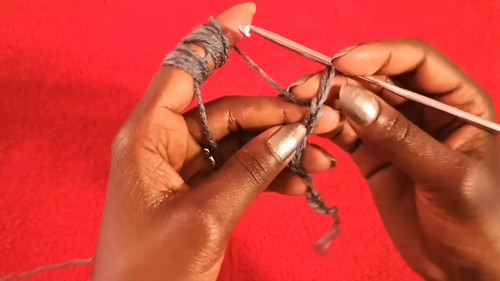 Hands working a grey foundation chain on a white hook against a red surface