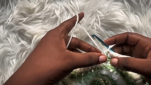 White foundation chain being started with a teal crochet hook on a white fur surface