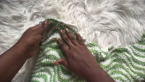 Hands smoothing a green and cream chevron crochet panel flat on a white fur surface
