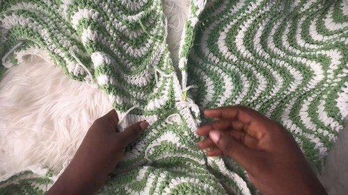 Green and cream chevron crochet sweater panels being seamed together with a yarn needle