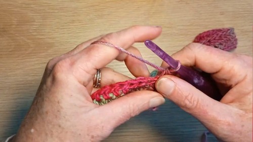 Hands working the first rows of a pink variegated crochet sweater neckband with a purple hook