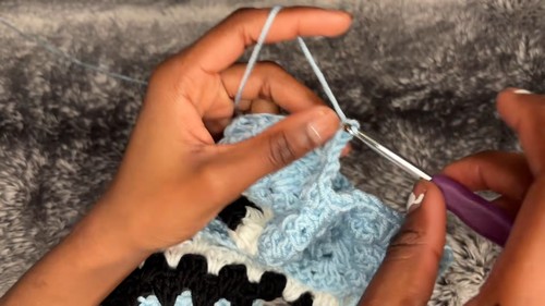 Working yarn pulled through a loop while joining light blue granny stitch fabric with a purple handled hook