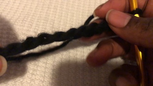Hands working a gold hook through a black foundation chain on a textured white surface