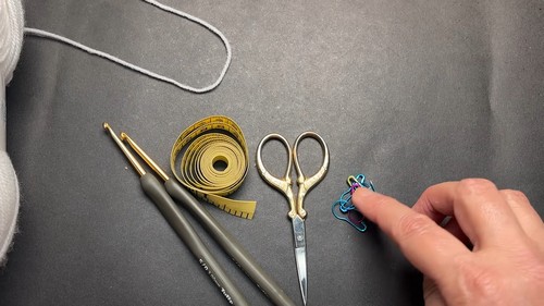Crochet hooks tape measure scissors and stitch markers laid out on a gray surface as project tools