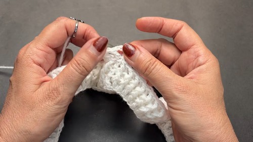 Close up of hands pinching the beginning rows of a white crochet yoke showing the tight double crochet base