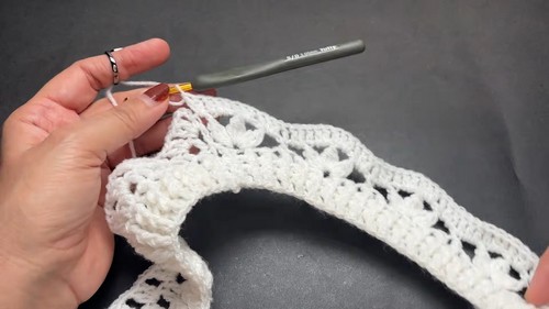 Hand working a gray hook through a white lace shell stitch strip showing the scalloped edge forming