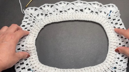 Hands holding a white top down crochet yoke worked in the round showing the open neckline and lace edging