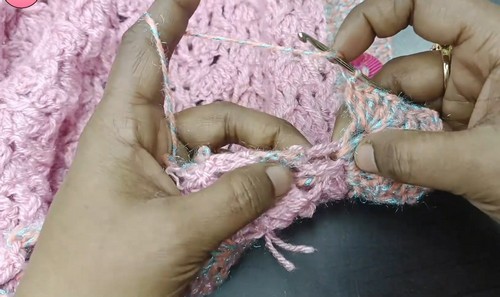 Hands seaming the edge of a pink crochet vest panel with a hook and yarn showing the joining technique in progress