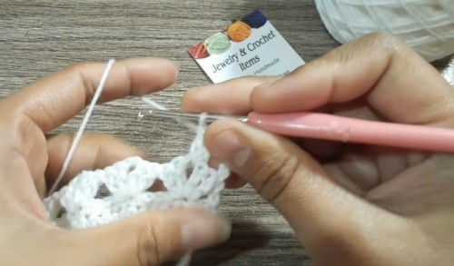 Crocheting an open lace row along the growing white collar edge with a pink hook