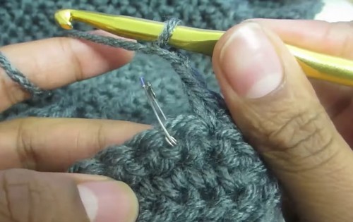 Yarn needle and gold hook used together on grey crochet fabric during construction