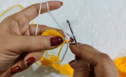 Hands joining yellow yarn to a finished white shell motif with a small hook to begin the next color row