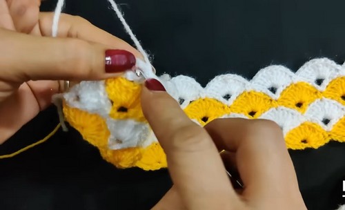 Hands working the beginning rows of a yellow and white shell stitch crochet strip showing the fan edges forming