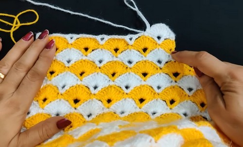 Hands smoothing a yellow and white two color crochet shell stitch panel showing the scalloped row texture