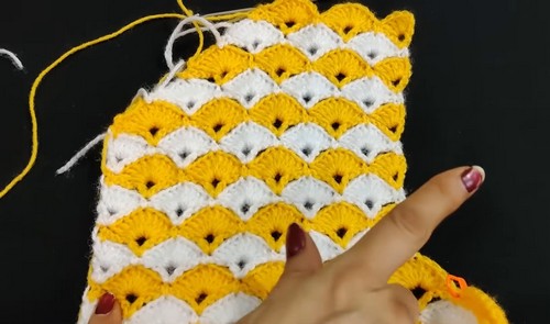 Hand holding a yellow and white crochet swatch showing alternating fan shaped shell rows in two color stripe